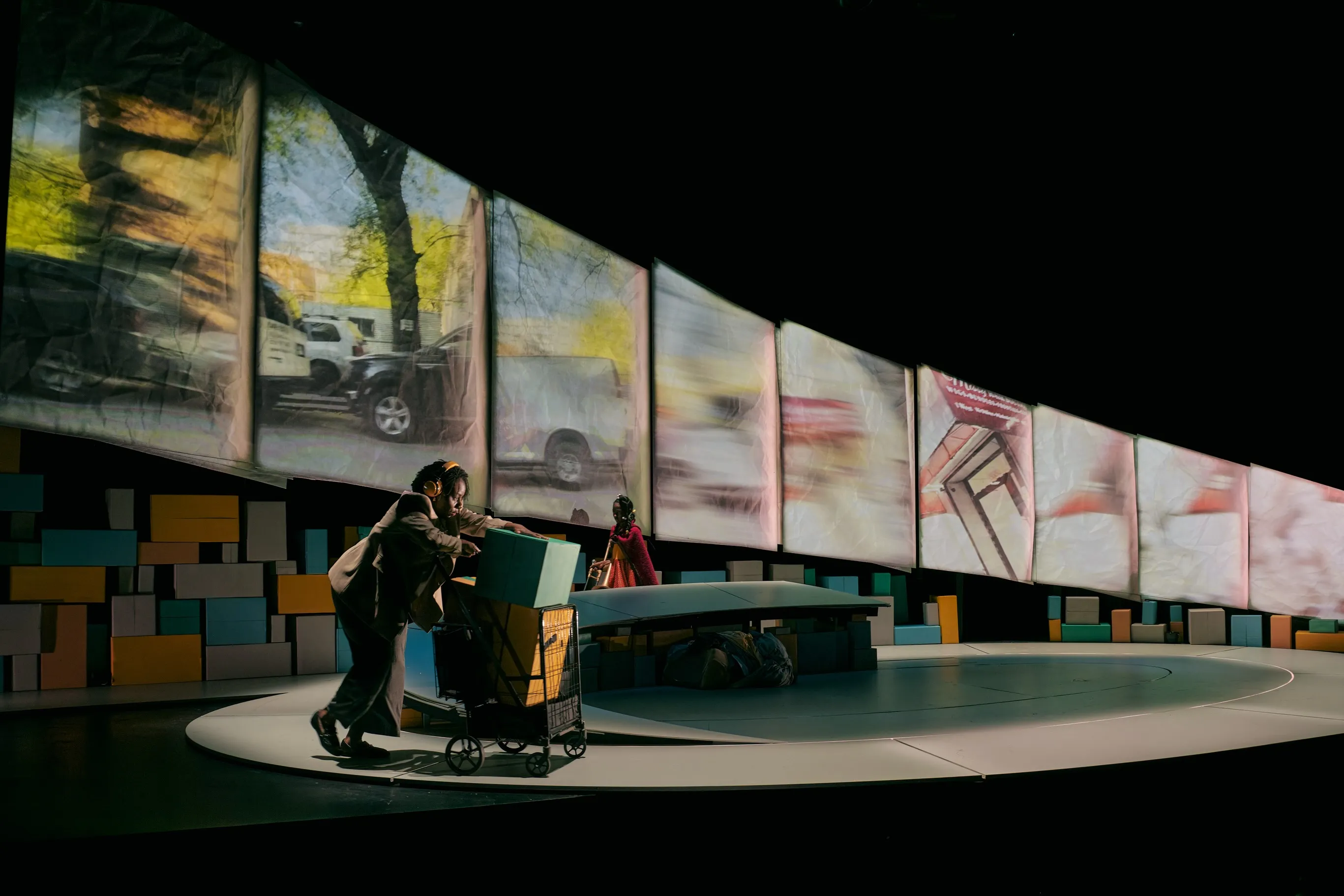 Abigail C. Onwunali in Creation Stories, mid-stride pushing a cart, projected traffic panels sweeping behind her