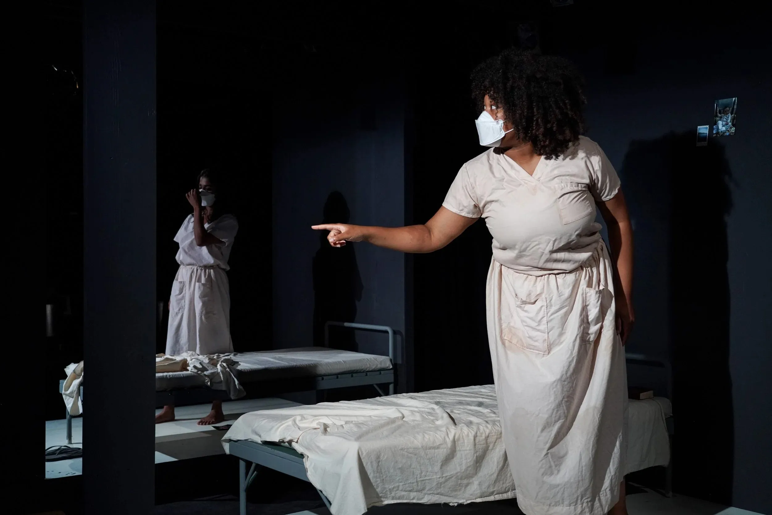 Performers in white on a dark stage lined with hospital beds, one pointing across the room, in #4 at the Yale Cabaret